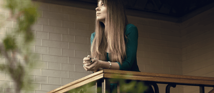 A woman leans on the railing of her balcony