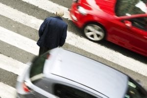 An elderly man walks across a street in heavy traffic