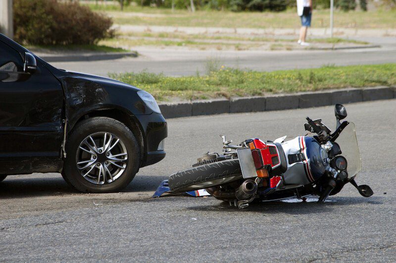 After an accident a motorcycle lies in the street next to a damaged car