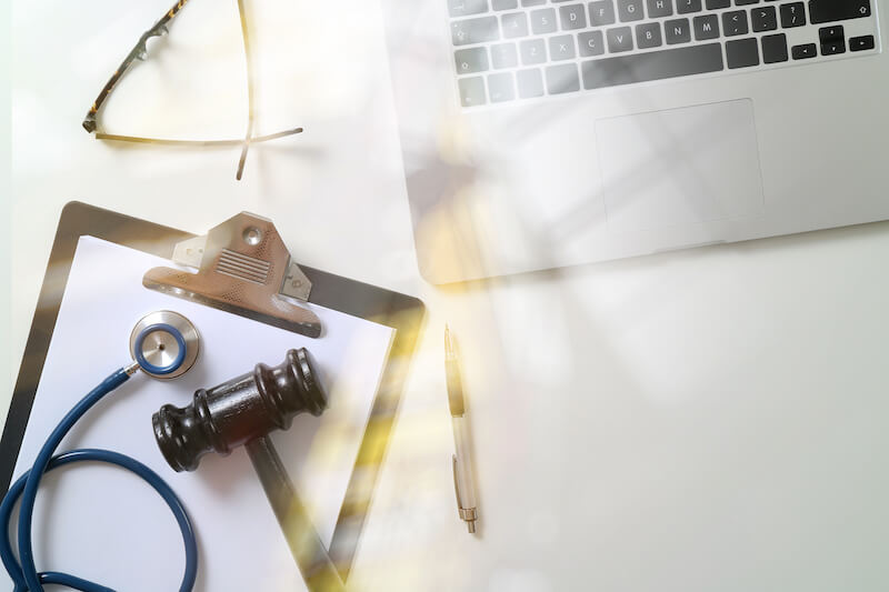A stethoscope and a gavel rest on a notepad next to a laptop on a desk