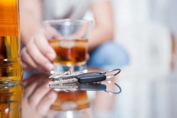 Hand holding a mixed drink on a table with car keys sitting next to it