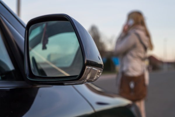 A close-up of a car approaching a lady walking across the street talking on the phone.