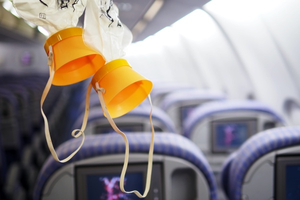 A pair of oxygen masks coming down from the storage compartment in an airplane.