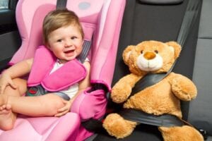 A child sitting in a car seat with a teddy bear next to her.