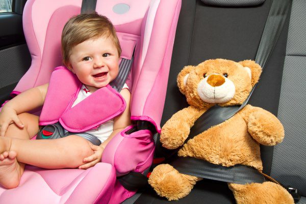 Una niña sentada en un asiento de carro con un oso de peluche a su lado.